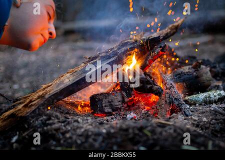 Donna che soffia un fuoco con scintille in foresta campeggio all'aperto Foto Stock