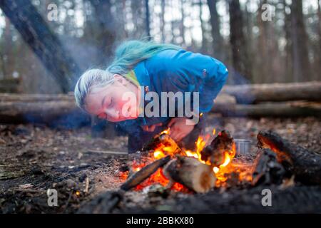 Donna che soffia un fuoco con scintille in foresta campeggio all'aperto Foto Stock