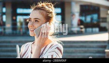 Businesswoman caucasico con frane e capelli rossi che parlano al telefono mentre camminano fuori Foto Stock