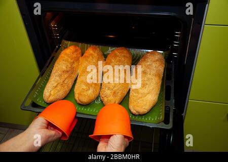 Il pane fatto in casa su una teglia viene estratto dal forno. Pane lungo, baguette a casa in cucina. Prodotti da forno. Cucinare a casa. Foto Stock
