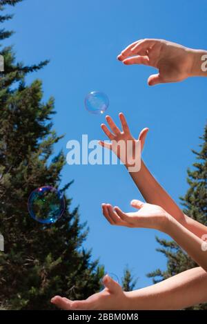 Bolle di sapone nei bambini mani contro un cielo blu Foto Stock