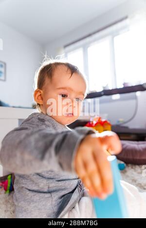 Ritratto di una bambina di un anno all'interno in una stanza luminosa giocando da sola Foto Stock