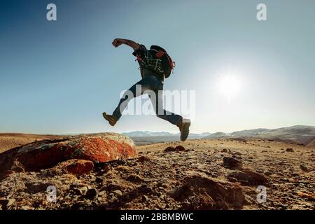 Escursionista o viaggiatore con zaino salta su grande roccia contro blu tramonto cielo Foto Stock