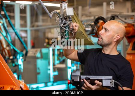 Ingegnere che esegue la manutenzione per bracci robot automatici in fabbrica automobilistica intelligente, concetto industriale Foto Stock