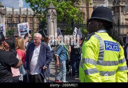 Il poliziotto guarda da lontano, come una manifestazione di protesta di "chiusura dell'operazione" si svolge alle porte della Camera del Parlamento di Londra. Foto Stock