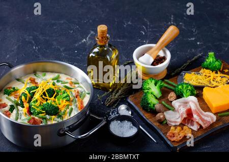 primo piano di deliziosa zuppa di panna con broccoli, fagiolo verde, pancetta fritta e formaggio cheddar grattugiato in una casseruola di metallo su un tavolo di cemento con la lavorazione Foto Stock