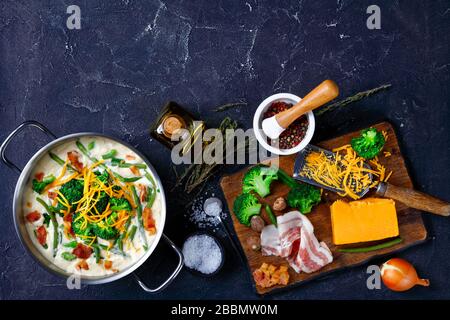 primo piano di deliziosa zuppa di panna con broccoli, fagiolo verde, pancetta fritta e formaggio cheddar grattugiato in una casseruola di metallo su un tavolo di cemento con la lavorazione Foto Stock