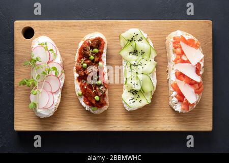 Quattro panini con verdure fresche, ravanelli, pomodori, cetrioli e microgreens su sfondo nero. Vista dall'alto. Foto Stock