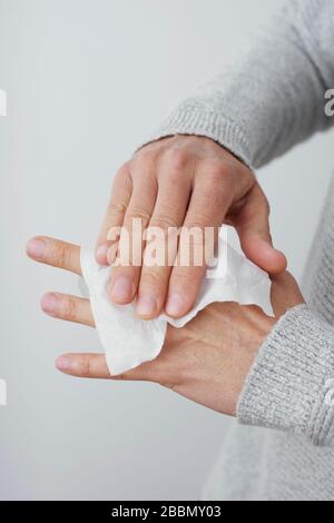 closeup di un uomo caucasico, indossando un maglione casual grigio chiaro, pulendo le mani con un panno disinfettante Foto Stock