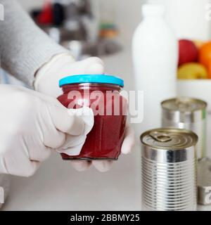 primo piano di un uomo in cucina, indossando guanti in lattice, pulendo lattine e vasetti per alimenti, appena acquistati, con un panno disinfettante Foto Stock