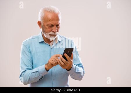 Ritratto dell'uomo anziano che sta inviando messaggi sullo smartphone. Foto Stock