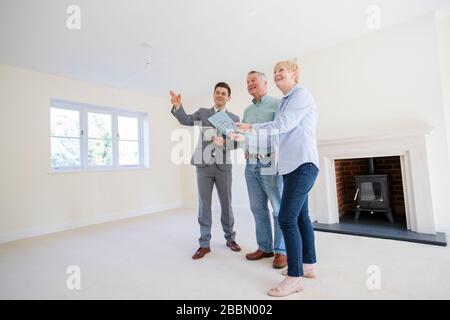 Realtor con il tablet digitale che mostra la coppia senior che cerca di ridurre le dimensioni intorno a casa di pensionamento Foto Stock