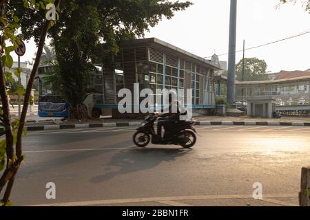 Giacarta, Indonesia - 13 luglio 2019: Un motociclista passa di fronte alla fermata dell'autobus dal sistema di trasporto pubblico TransJakarta. Foto Stock