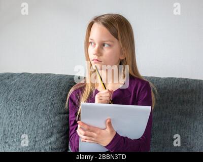 Una ragazza è seduta su un divano e sta pensando a che cosa scrivere con una matita sulle note della carta Foto Stock