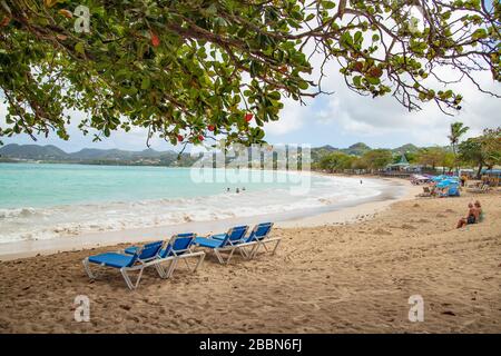 Castries, Santa Lucia - 8 Febbraio 2020: Turista a Vigie spiaggia - persone sotto FLUSSO ombrelloni sponsorizzati, coppia seduta su sabbia, sedie a sdraio. Foto Stock