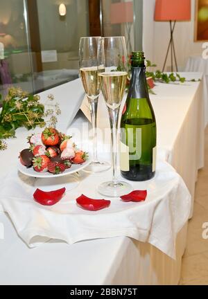 Bottiglia di champagne, due bicchieri e fragole al cioccolato su un vassoio con petali di rosa Foto Stock