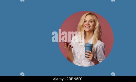 Ritratto di una giovane donna soddisfatta usando il telefono mobile mentre tiene una tazza di caffè per andare. Pianto del classico foro circolare blu nella parete. Fare Foto Stock