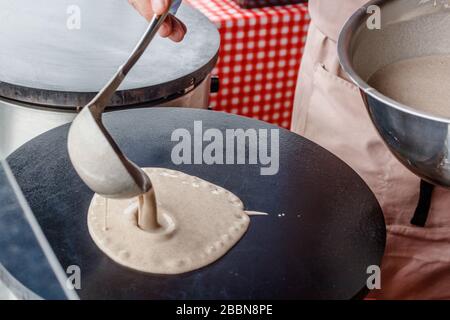 Fare crepes frittelle in un mercato alimentare. Una mano sta versando pastella su una sporcizia di metallo all'esterno Foto Stock