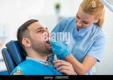 Ritratto di paziente maschio che ha trattamento al dentista. Dentista che esamina i denti di un paziente nell'ufficio dentista. Foto Stock