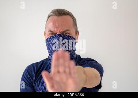 L'uomo che indossa una protezione del viso contro il Coronavirus o Covid-19 che tiene la mano facendo rispettare le distanzazioni sociali per prevenire la diffusione della pandemia Foto Stock