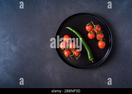 Flta Lay view pomodoro rosso ciliegia e pepe verde servito su piatto nero su sfondo nero. Foto Stock