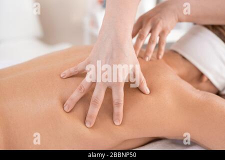 Primo piano di massaggio terapista coccole muscoli posteriori della donna mentre si esegue il massaggio manuale nel salone spa Foto Stock