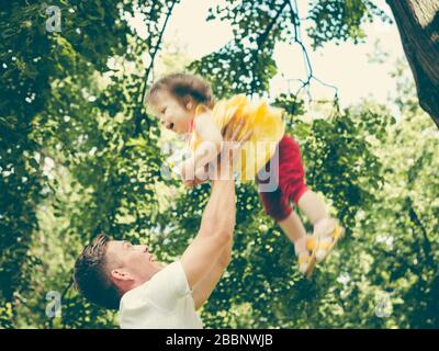 Papà e la sua bambina di un anno si divertono. Padre getta la sua bambina. Immagine colorata per il concetto moderno di famiglia Foto Stock