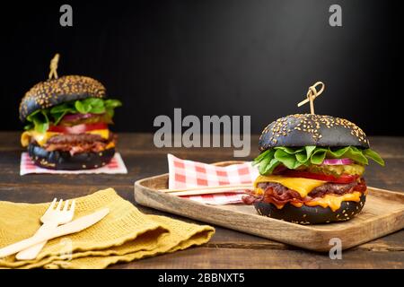 Due hamburger neri succosi su sfondo di legno scuro Foto Stock