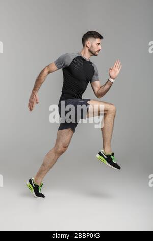 Immagine di giovane atletico in corsa sportswear mentre si lavora isolato su sfondo grigio Foto Stock