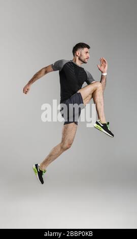 Immagine del giovane atletico in salto sportswear mentre si lavora isolato su sfondo grigio Foto Stock