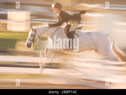 Sfocatura stilizzata del movimento di giovani donne equestri che si esibiscono in show horse jumping evento Foto Stock