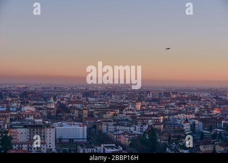 La vista della città di Bergamo al tramonto dalle mura della città alta, con un aereo decollare Foto Stock