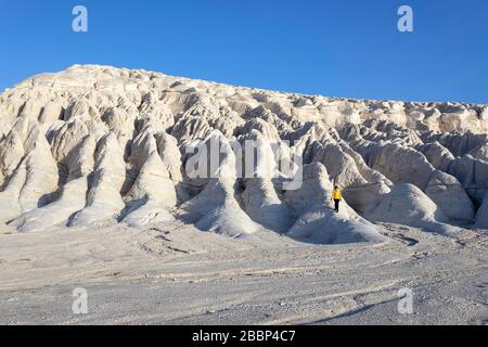Donna in giacca gialla in piedi su formazioni rocciose bianche nel paesaggio suggestivo del lago salato di Tuzbair, Aktau, Mangystau, Kazakhstan, Foto Stock