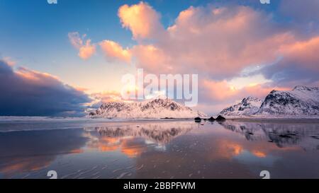 Il cielo colorato si riflette nell'acqua sulla spiaggia con la montagna innevata sullo sfondo Foto Stock
