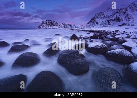 Onde di mare lavando sopra le rocce sulla spiaggia innevata. Foto Stock