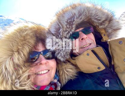Primo piano di una coppia vestita in parkas con cappe di pelliccia fuori per una passeggiata nel sole d'inverno Foto Stock
