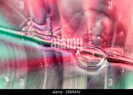 Liquido colorato rosso e verde traslucido con bolle d'aria che gocciolano su una parete di vetro trasparente e formano un pozza luminoso. Foto Stock