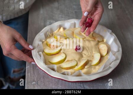 La padrona di casa sta preparando la mela charlotte in cucina. Mette il bacche su una torta di mele in un piatto da forno. Pasta di mele cruda Foto Stock