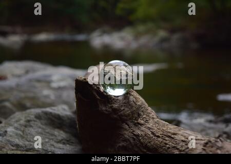 Piccola Crystal Ball arroccata su un Log on Rocky Riverbank Foto Stock