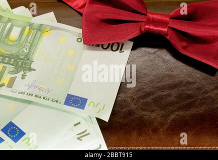soldi in una busta su uno sfondo marrone del blocco note e cravatta rossa della prua Foto Stock