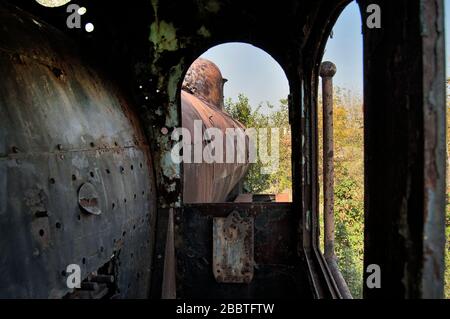 Vecchia locomotiva a vapore della ferrovia disfunzionale che è overgrown con erbacce. Foto Stock