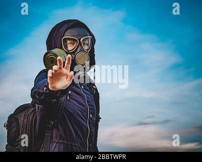 Ragazza in una maschera di gas nero e vestiti scuri con una cappa nel pomeriggio contro il cielo. La ragazza tiene fuori la sua mano come un avvertimento e una richiesta per hel Foto Stock