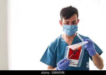 Il tecnico sanitario medico che tiene il kit di prelievo COVID 19 con tampone, indossando maschera protettiva bianca e guanti Foto Stock