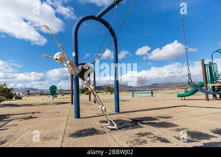 Scheletro che gioca superman su un bambino swing in un parco vuoto Foto Stock