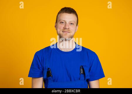 Ritratto di un lavoratore maschile in tute. Giovane tecnico con capelli rossi su sfondo giallo. Foto Stock