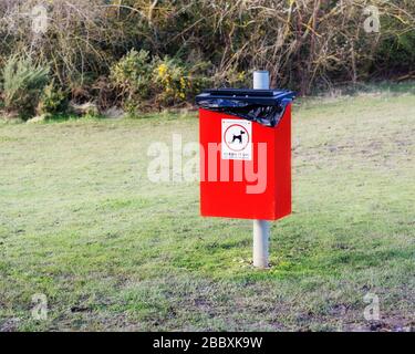 Cestino di rifiuti rosso per la figliata del cane con il segno pulirlo in su e un'immagine di un cane nel parco Foto Stock