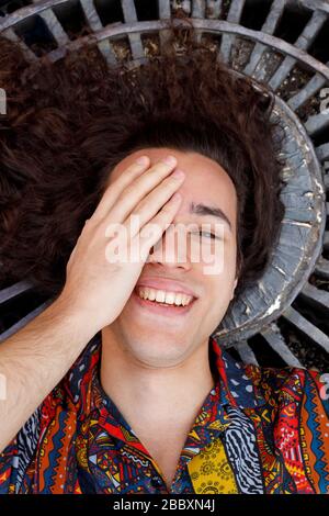 Attraente giovane uomo sorridente e coprente un occhio con la sua mano Foto Stock