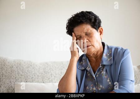 Vecchia donna asiatica seduta sul divano e avere un mal di testa a casa. Concetto di assistenza sanitaria di alto livello. Foto Stock