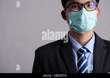 Primo piano di un uomo d'affari in un vestito che indossa maschera protettiva del viso, preparati per Coronavirus e pm 2.5 lotta contro lo sfondo grigio. Co. Assistenza sanitaria Foto Stock