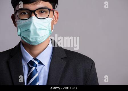 Primo piano di un uomo d'affari in un vestito che indossa maschera protettiva del viso, preparati per Coronavirus e pm 2.5 lotta contro lo sfondo grigio. Co. Assistenza sanitaria Foto Stock